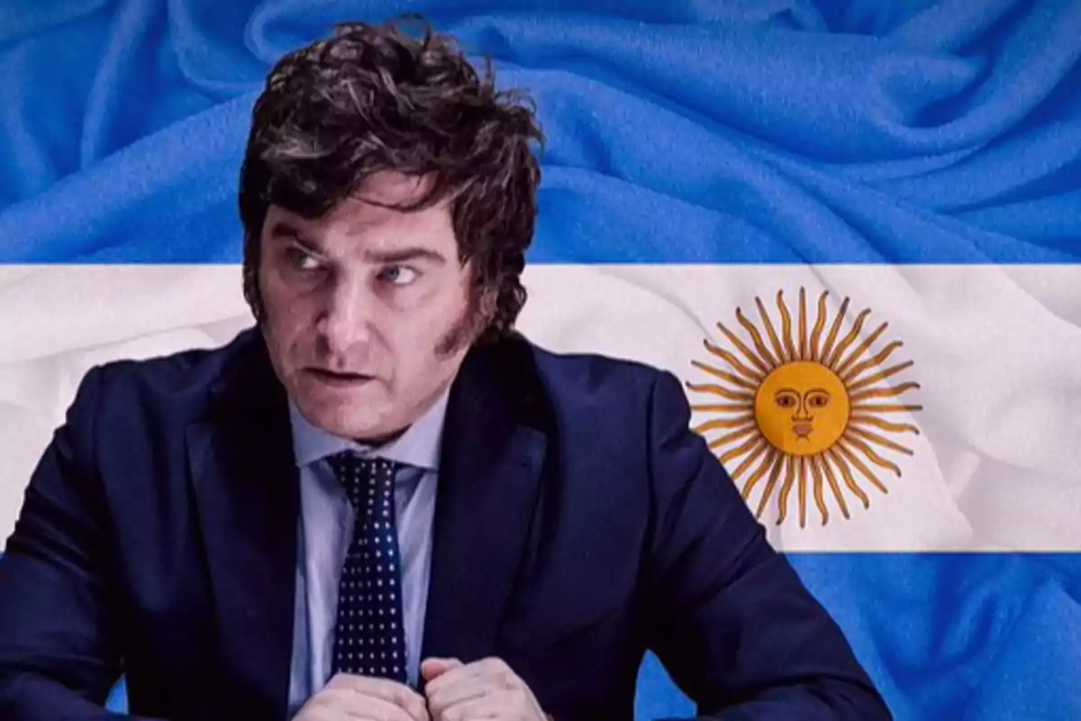 Un hombre con traje oscuro y corbata de lunares frente a una bandera de Argentina.