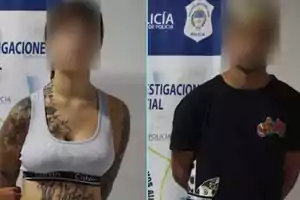 Dos personas con rostros difuminados posan frente a un fondo con logotipos de la policía.