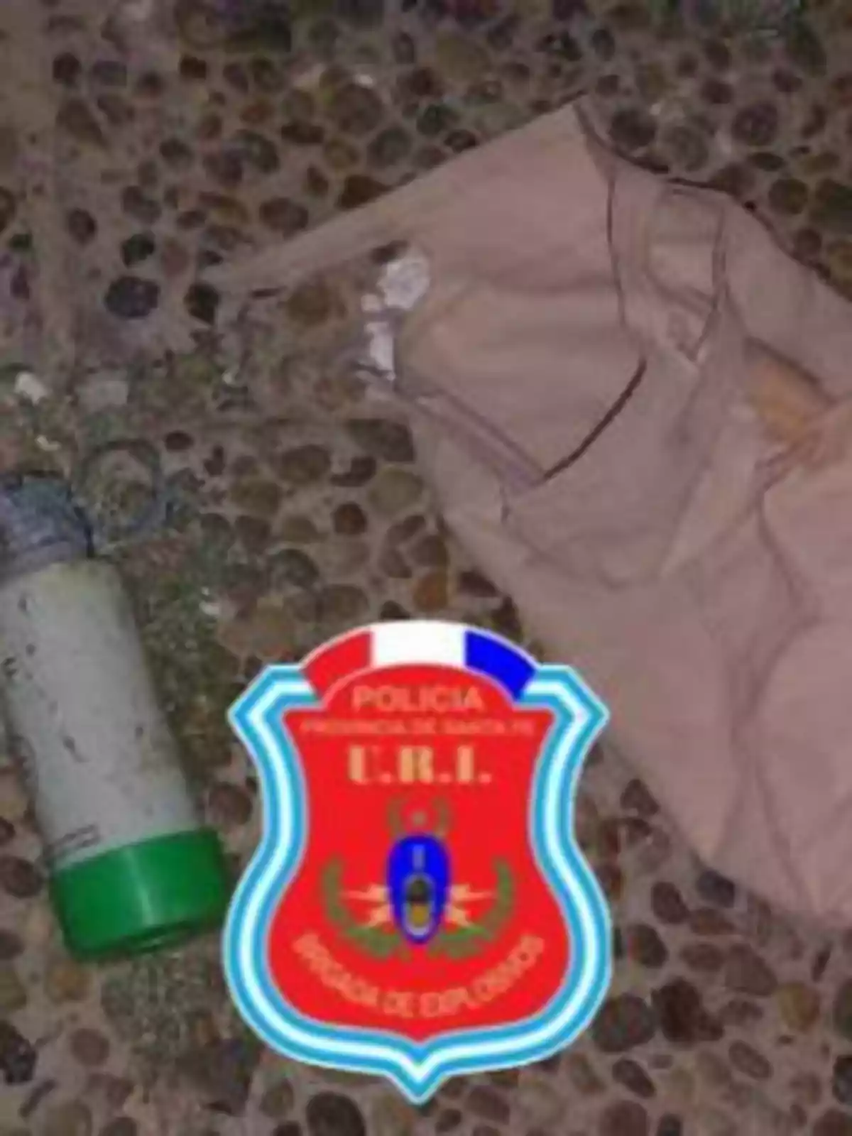 An image shows a bulletproof vest and a cylindrical object on the ground, next to a Santa Fe Province police shield, explosives brigade.