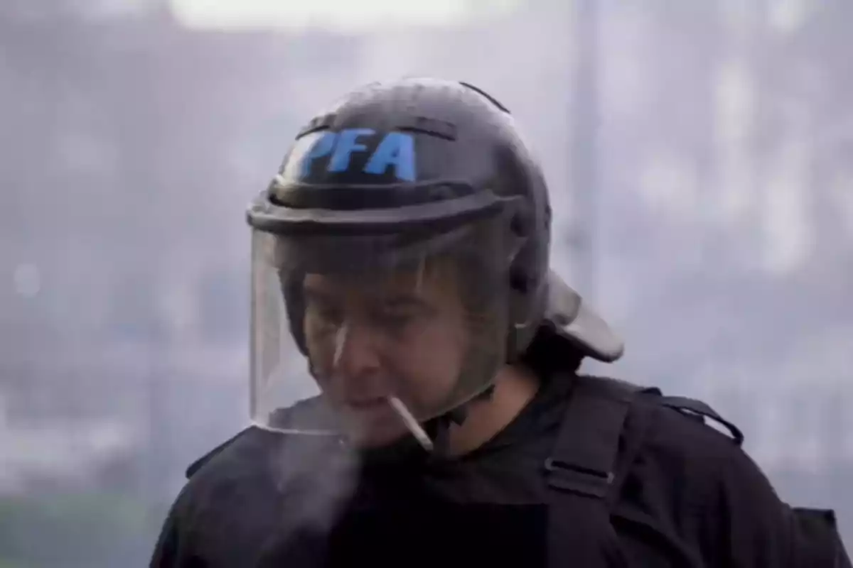 A police officer with a helmet and transparent visor smokes a cigarette while exhaling smoke.