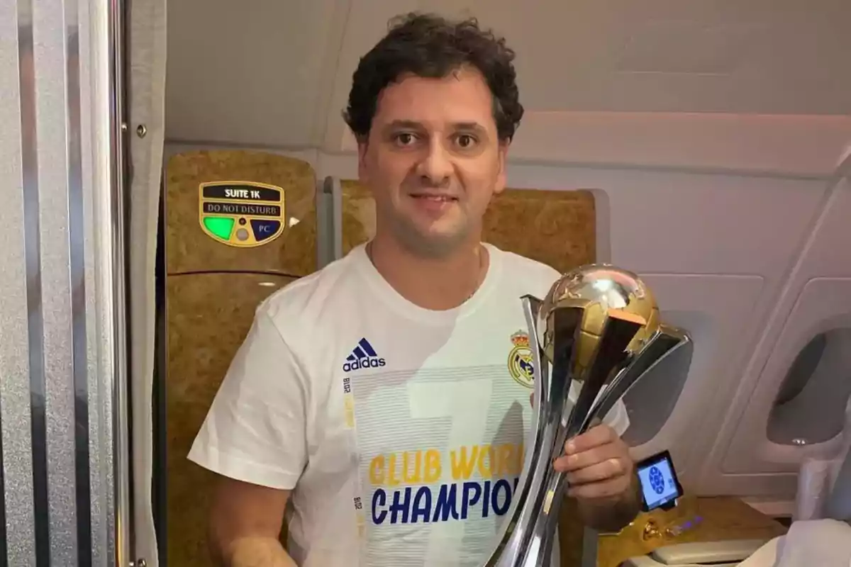 Hombre con camiseta de Real Madrid sosteniendo un trofeo dentro de un avión Hombre con camiseta de Real Madrid sosteniendo un trofeo dentro de un avión