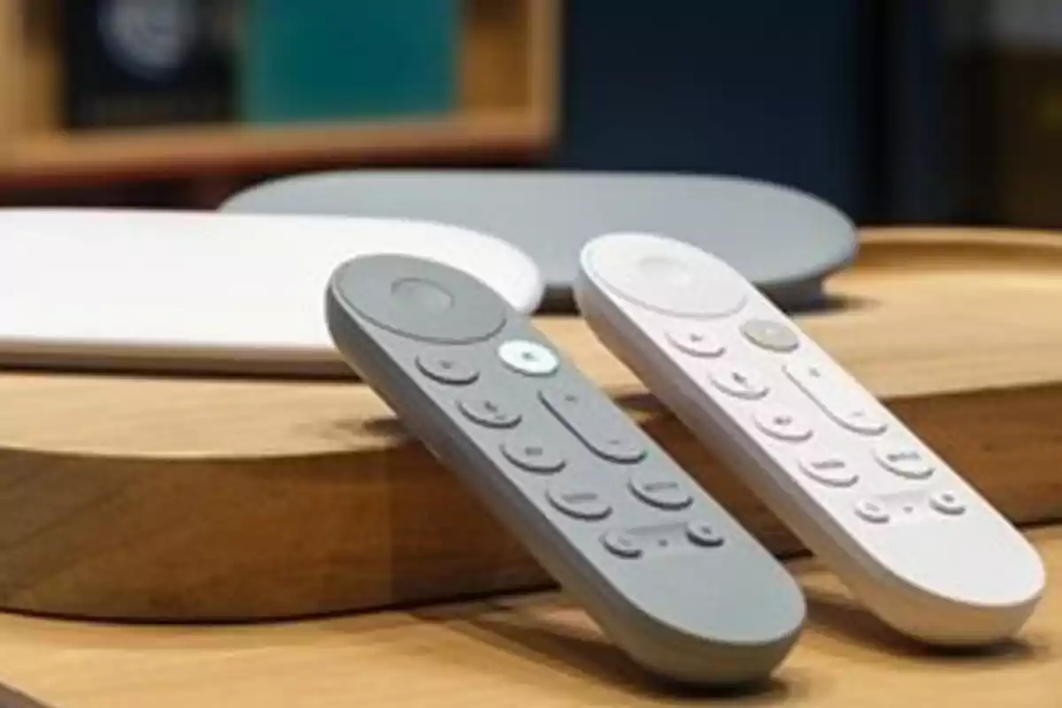 Two remote controls of different colors are resting on a wooden surface next to two rectangular electronic devices. Two remote controls of different colors are resting on a wooden surface next to two rectangular electronic devices.