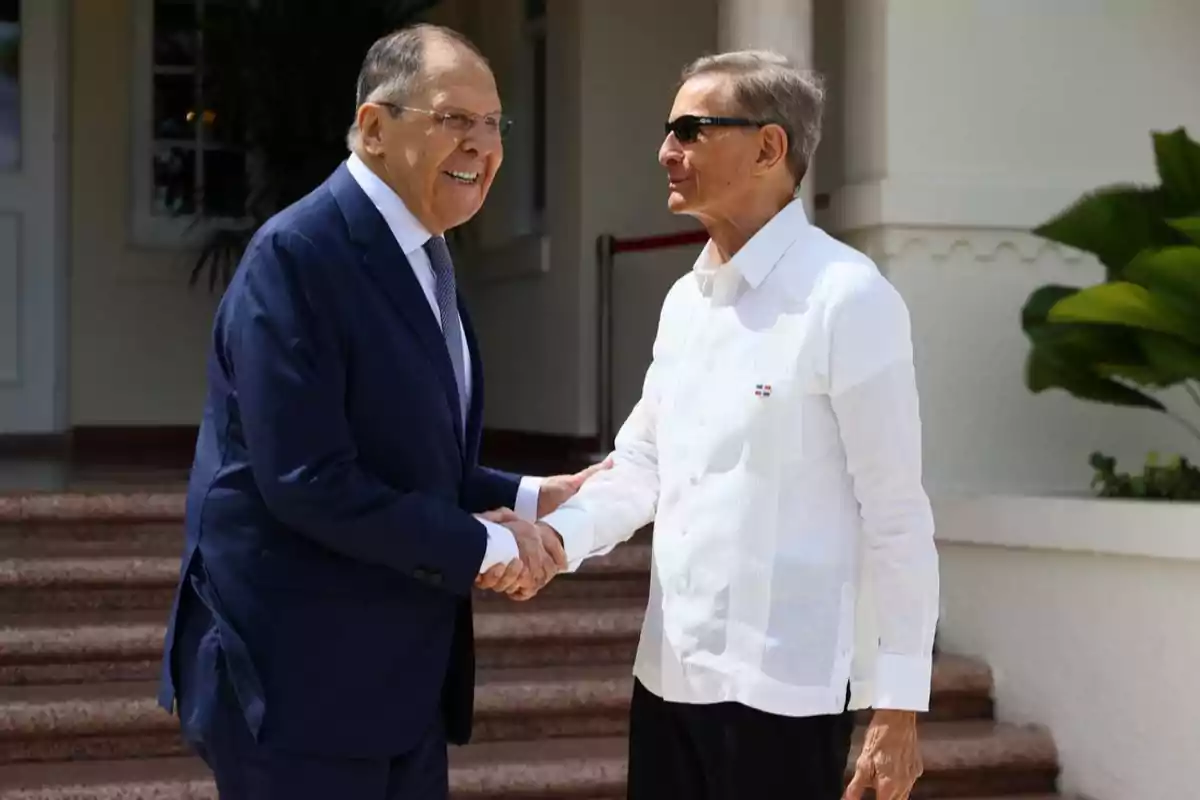 Dos hombres se saludan cordialmente con un apretón de manos en un entorno exterior elegante.