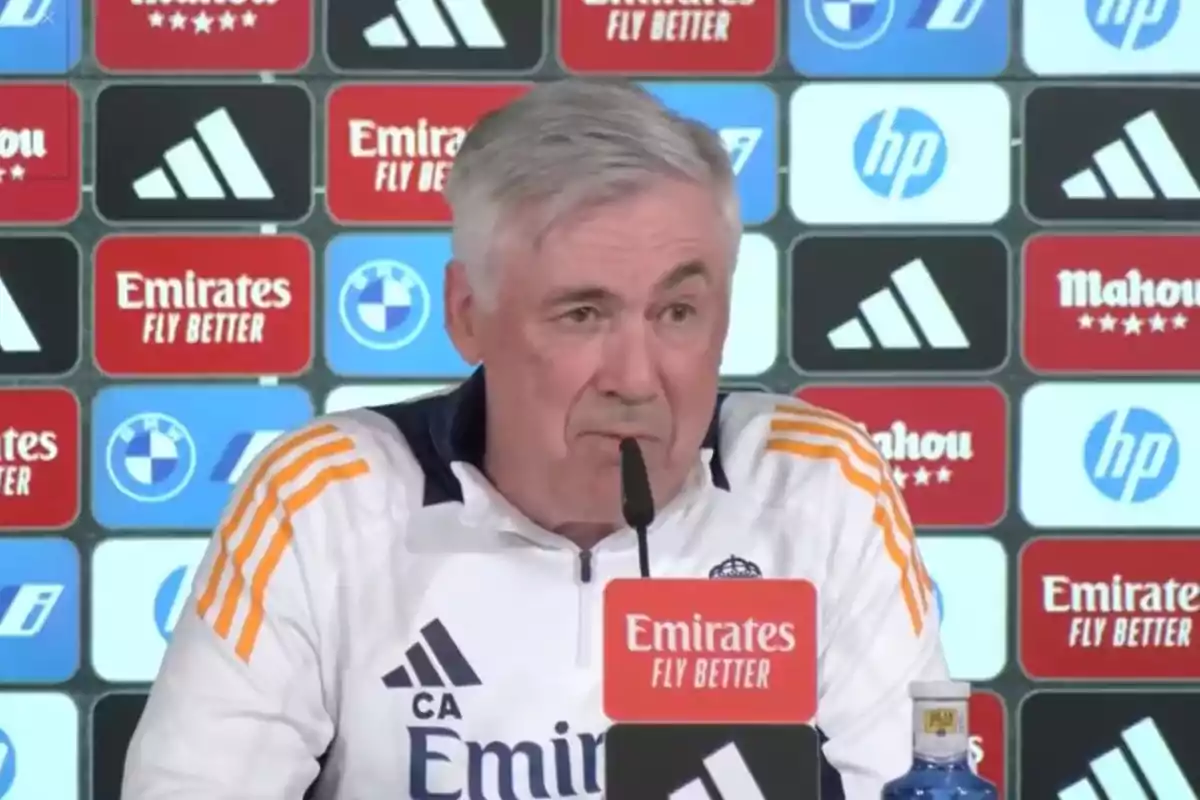 Un hombre de cabello canoso en una conferencia de prensa con un fondo de logotipos de marcas.