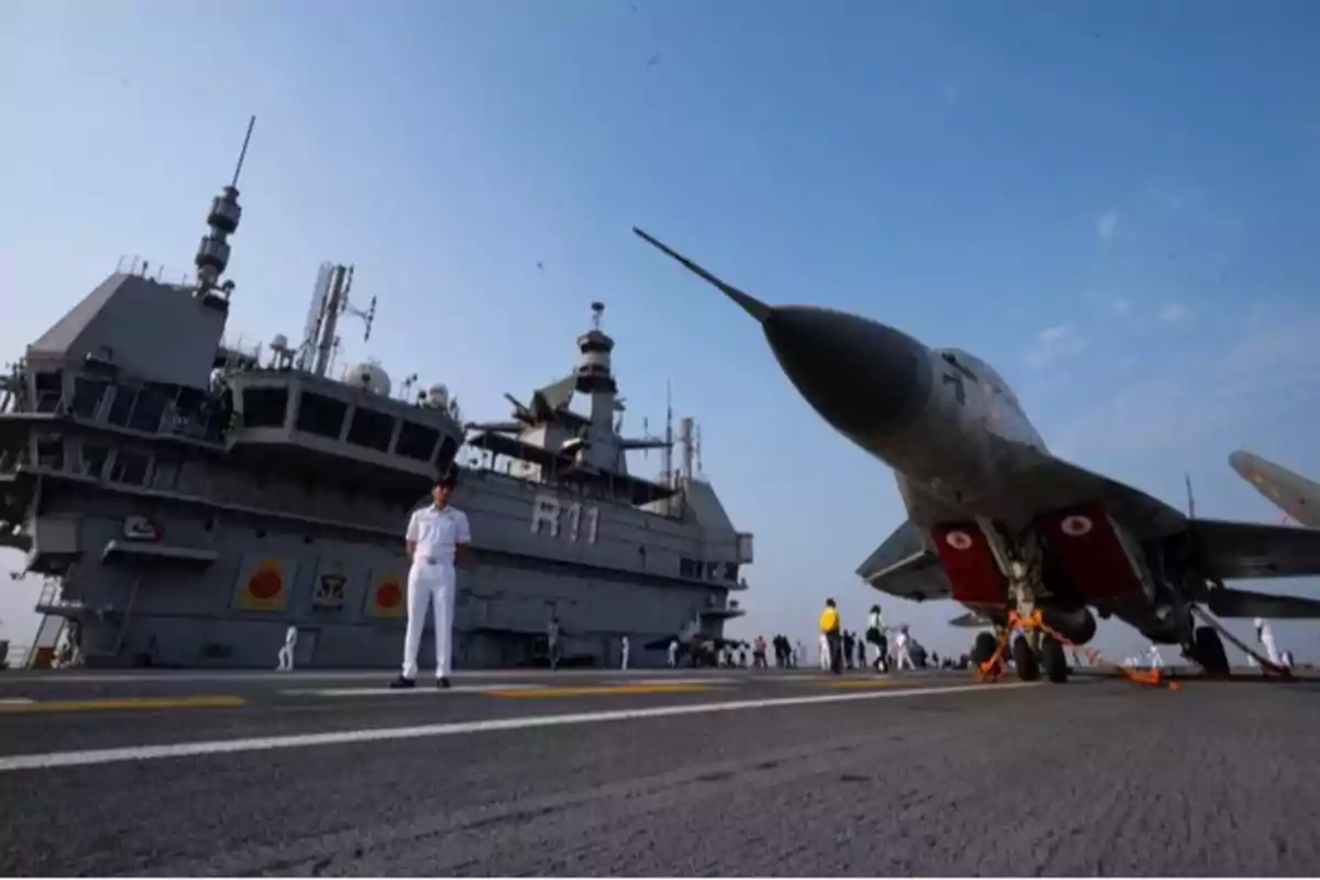 An aircraft carrier with a fighter jet on the deck and military personnel around.
