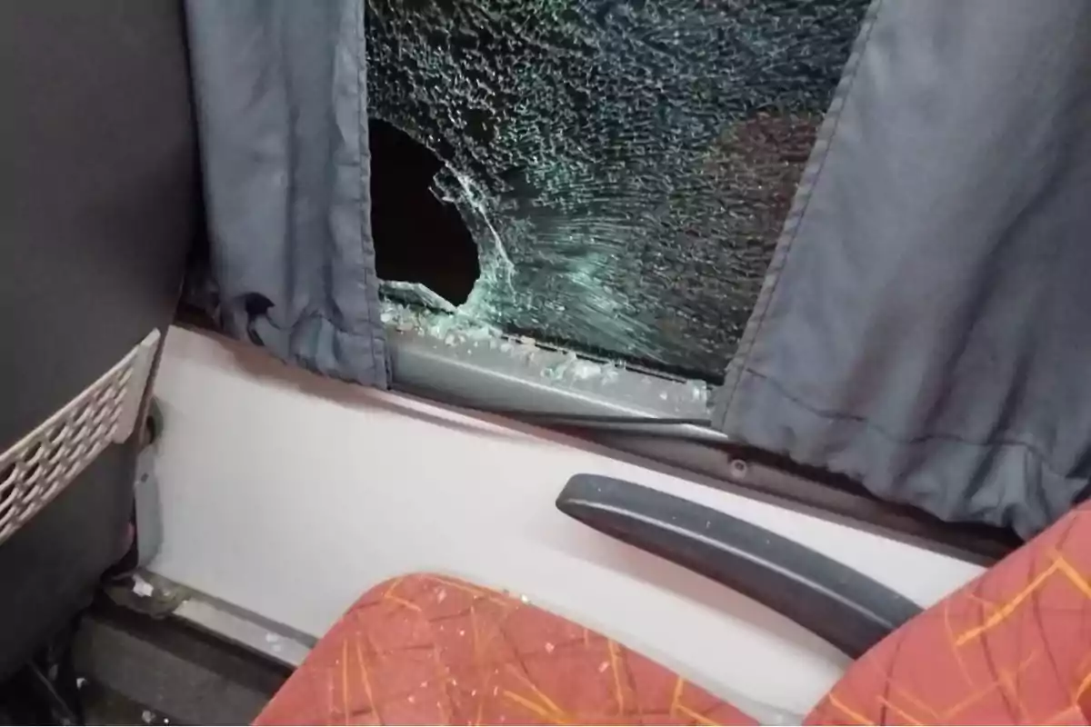 Ventana rota de un autobús con cortina azul y asiento naranja. Ventana rota de un autobús con cortina azul y asiento naranja.