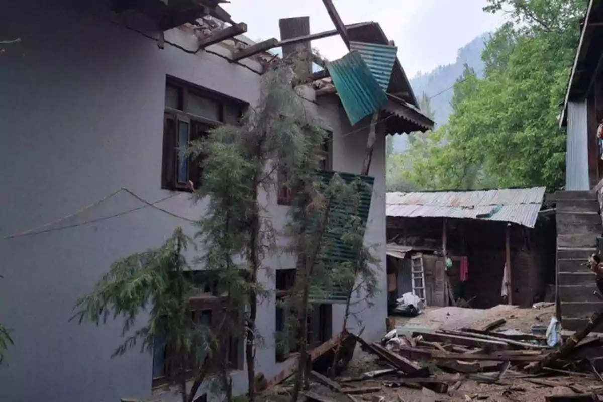 Damaged building with debris on the ground and partially collapsed roof, surrounded by trees and adjacent structures. Damaged building with debris on the ground and partially collapsed roof, surrounded by trees and adjacent structures.