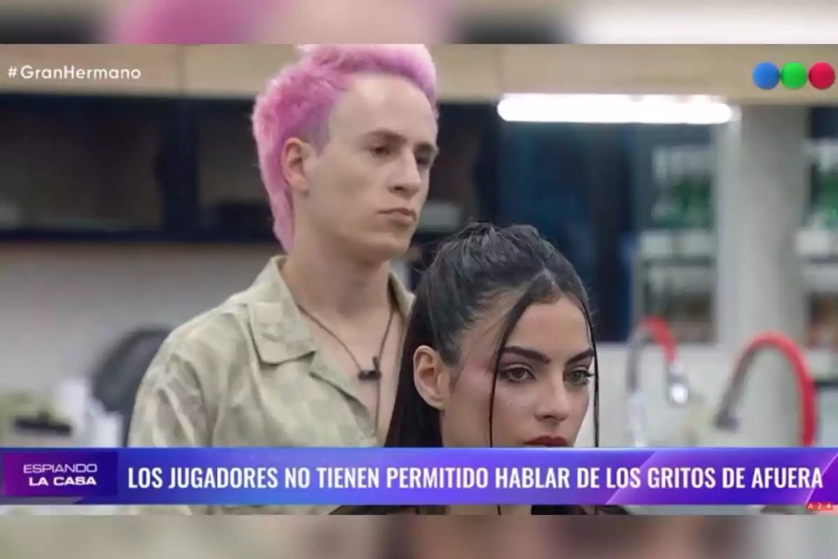 Dos personas están en una cocina, una de ellas tiene el cabello rosado y la otra cabello oscuro, con un texto en la parte inferior que dice que los jugadores no pueden hablar de los gritos de afuera. Dos personas están en una cocina, una de ellas tiene el cabello rosado y la otra cabello oscuro, con un texto en la parte inferior que dice que los jugadores no pueden hablar de los gritos de afuera.