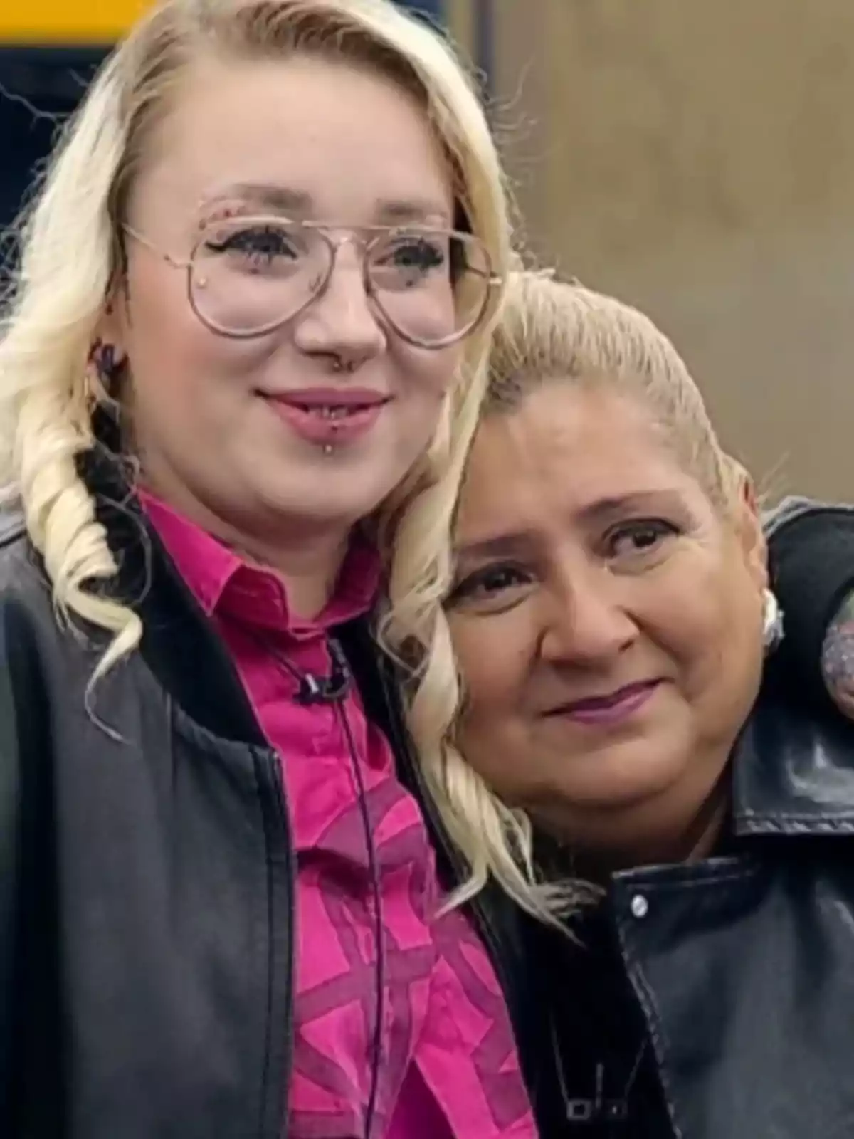 Two women hugging and smiling, one of them wearing large glasses and a pink jersey, the other resting her head on her shoulder, and both wearing dark jackets. Two women hugging and smiling, one of them wearing large glasses and a pink jersey, the other resting her head on her shoulder, and both wearing dark jackets.