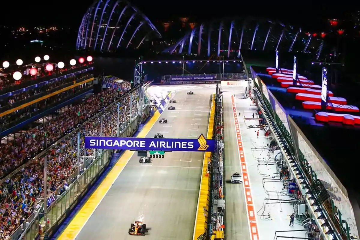 Vista nocturna de una carrera de Fórmula 1 en el circuito urbano de Singapur con público en las gradas y autos en la pista.