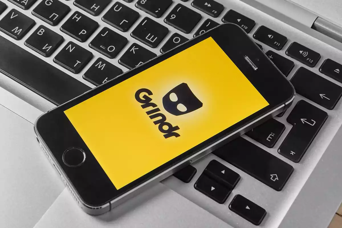Un teléfono móvil con la pantalla encendida mostrando el logo de Grindr sobre un teclado de computadora portátil Un teléfono móvil con la pantalla encendida mostrando el logo de Grindr sobre un teclado de computadora portátil
