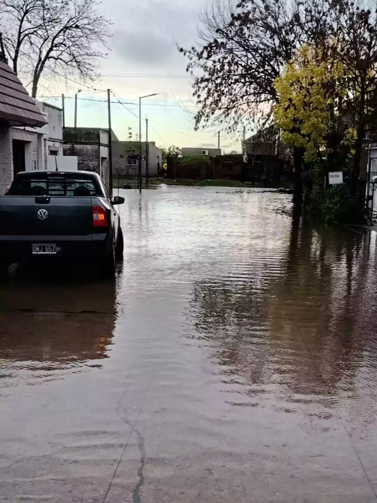 A flooded street with a parked car on the left and leafless trees on the sides. A flooded street with a parked car on the left and leafless trees on the sides.