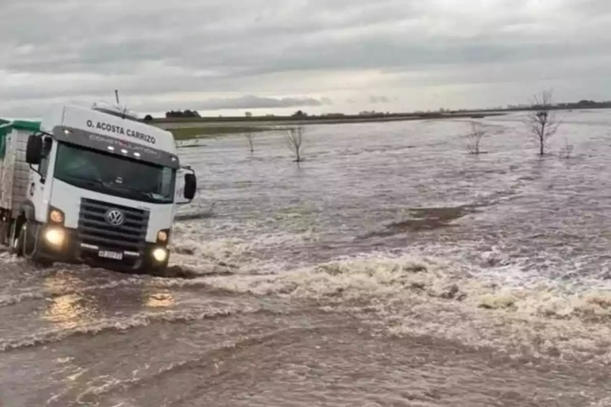 A truck drives through a flooded road with rapidly flowing water under a cloudy sky. A truck drives through a flooded road with rapidly flowing water under a cloudy sky.