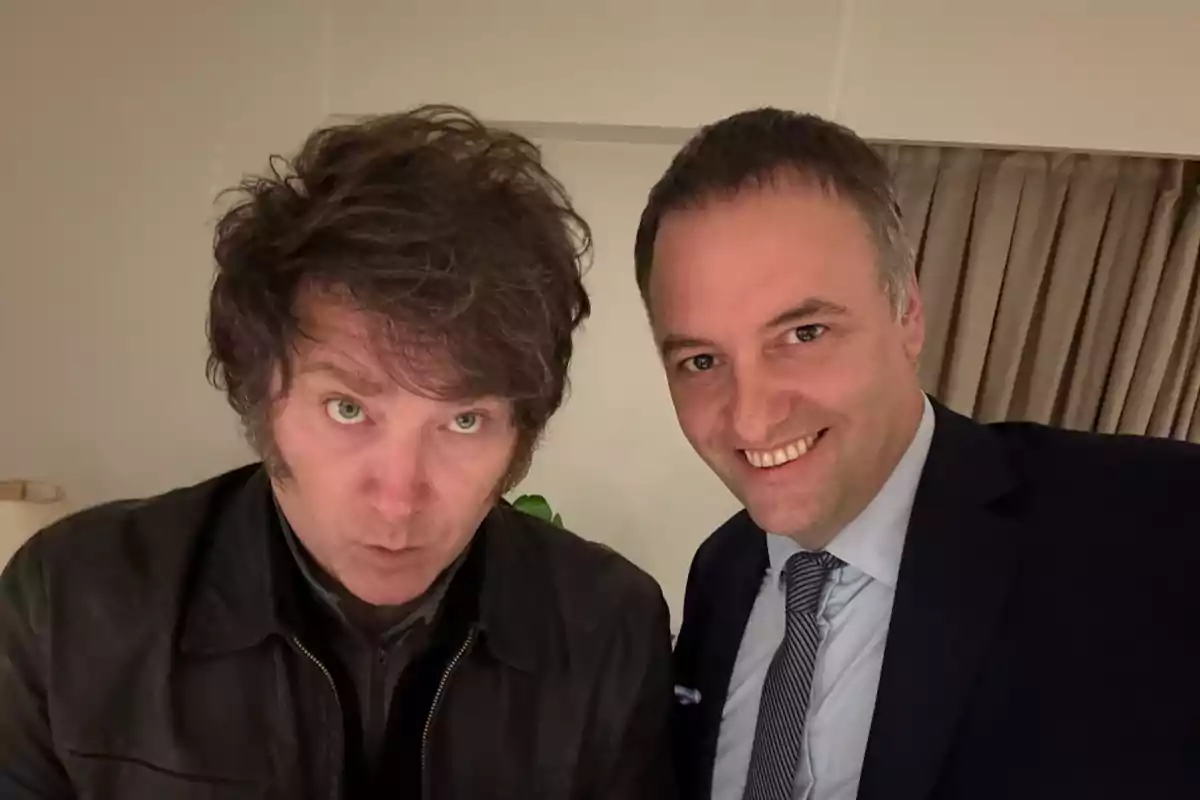 Dos personas posando para una selfie en un interior con cortinas de fondo.