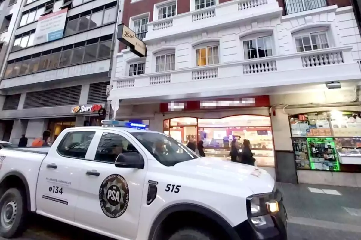 Una camioneta de la Policía de Seguridad Aeroportuaria está estacionada frente a un edificio de varios pisos con un hotel y tiendas en la planta baja.