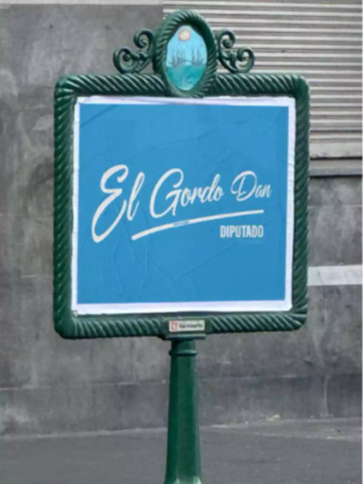Cartel azul en la calle con el texto El Gordo Dan diputado en letras blancas dentro de un marco verde Cartel azul en la calle con el texto El Gordo Dan diputado en letras blancas dentro de un marco verde