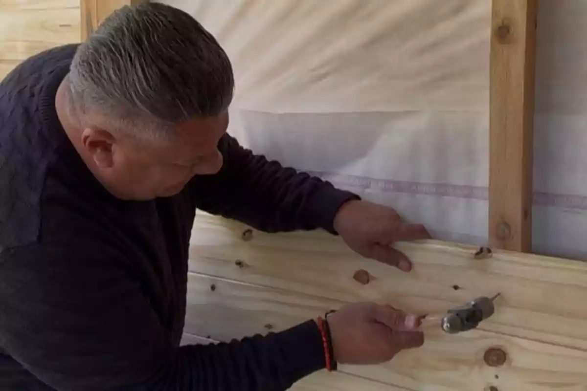 Hombre sujetando una tabla de madera mientras utiliza un taladro eléctrico