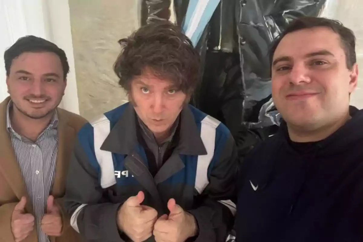 Three men pose for a selfie indoors; two of them are smiling and giving a thumbs up, while the one in the center also raises both thumbs but has a serious expression. Three men pose for a selfie indoors; two of them are smiling and giving a thumbs up, while the one in the center also raises both thumbs but has a serious expression.