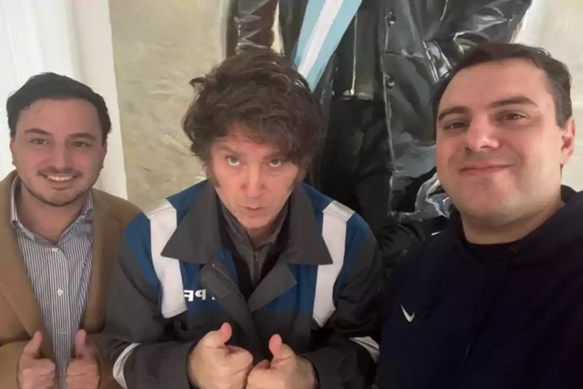 Three men pose for a selfie, smiling and giving a thumbs-up gesture in front of a painting.