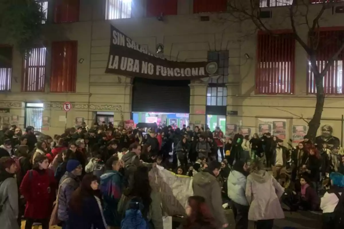 Manifestación de estudiantes frente a un edificio universitario con una pancarta que dice sin salarios la UBA no funciona