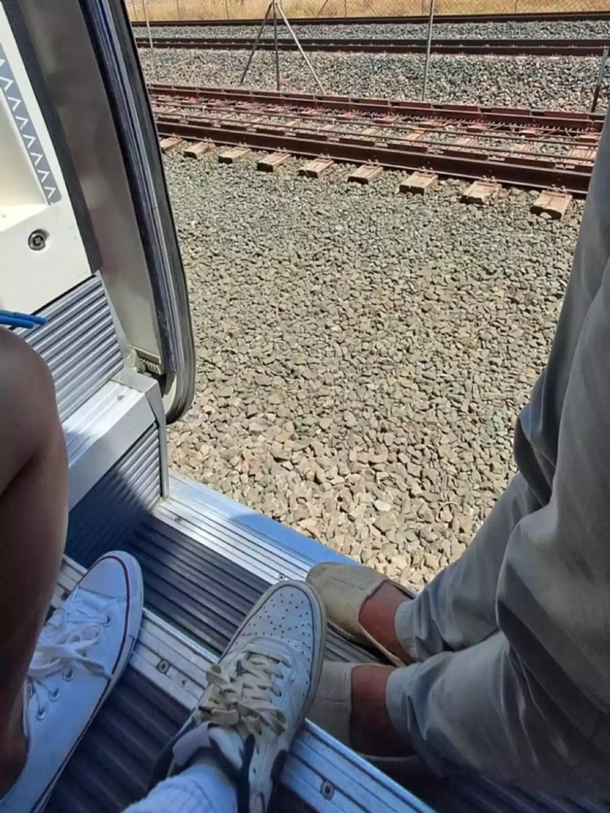 Personas sentadas en la puerta abierta de un tren con vista a las vías férreas.