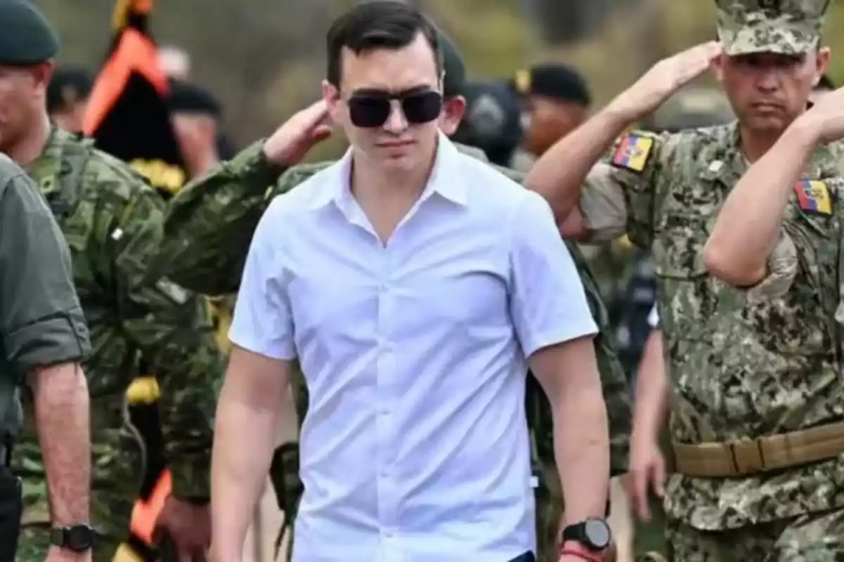 A man in a white jersey and sunglasses walks among saluting military personnel.