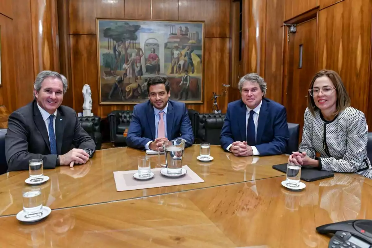 Cuatro personas sentadas alrededor de una mesa de madera en una sala de reuniones con paredes de madera y un cuadro grande en la pared de fondo.