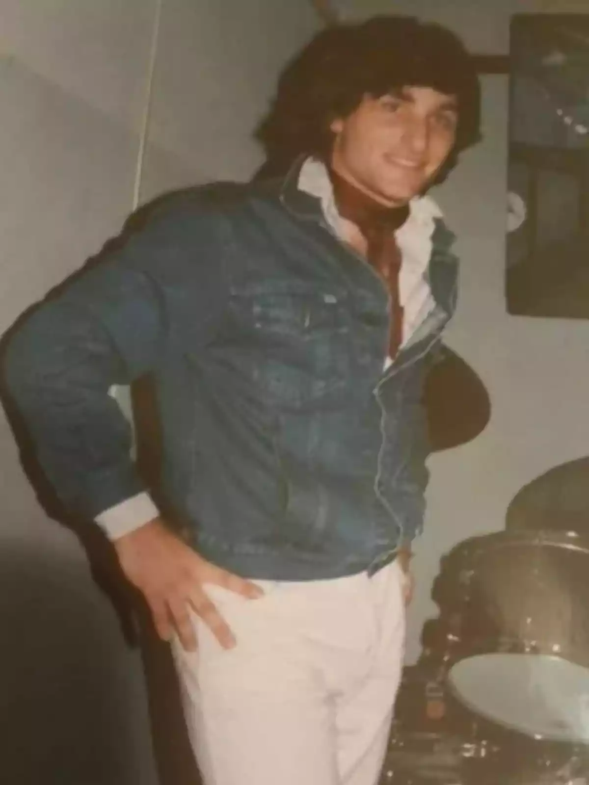Un hombre joven con chaqueta de mezclilla y pantalones claros posa junto a una batería. Un hombre joven con chaqueta de mezclilla y pantalones claros posa junto a una batería.