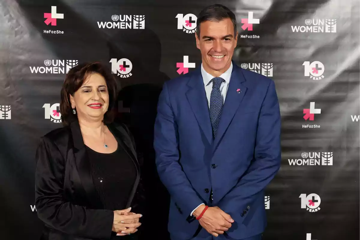 Dos personas posan frente a un fondo con logotipos de UN Women y HeForShe, celebrando el décimo aniversario de la iniciativa.