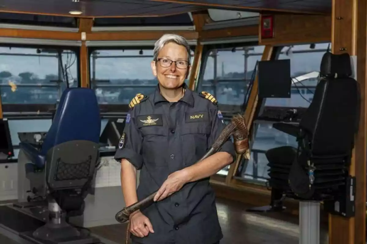 Una persona con uniforme de la marina sostiene un bastón ceremonial en el puente de mando de un barco.