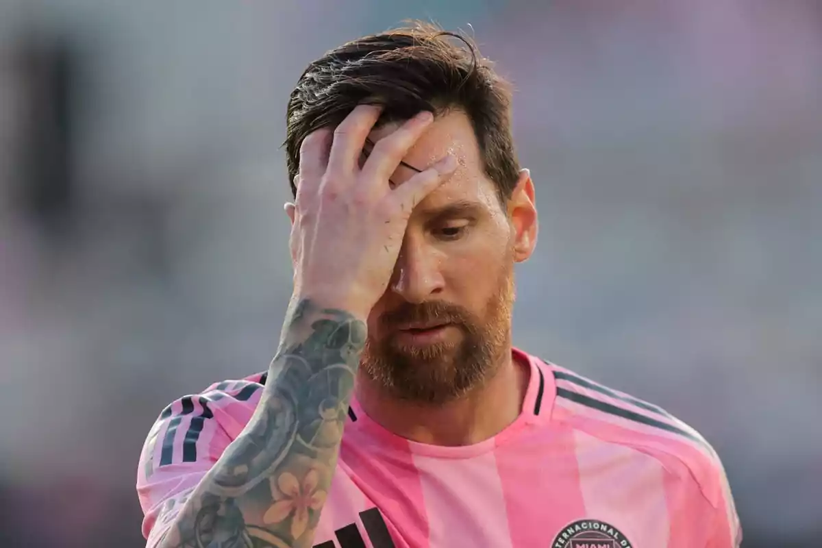 A player in a pink jersey puts his hand to his forehead in a gesture of concern or fatigue.