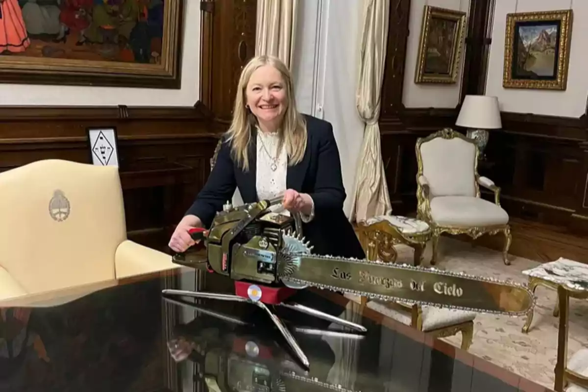 Una persona sonriente sostiene una motosierra decorativa en una elegante sala con muebles clásicos y cuadros en las paredes.