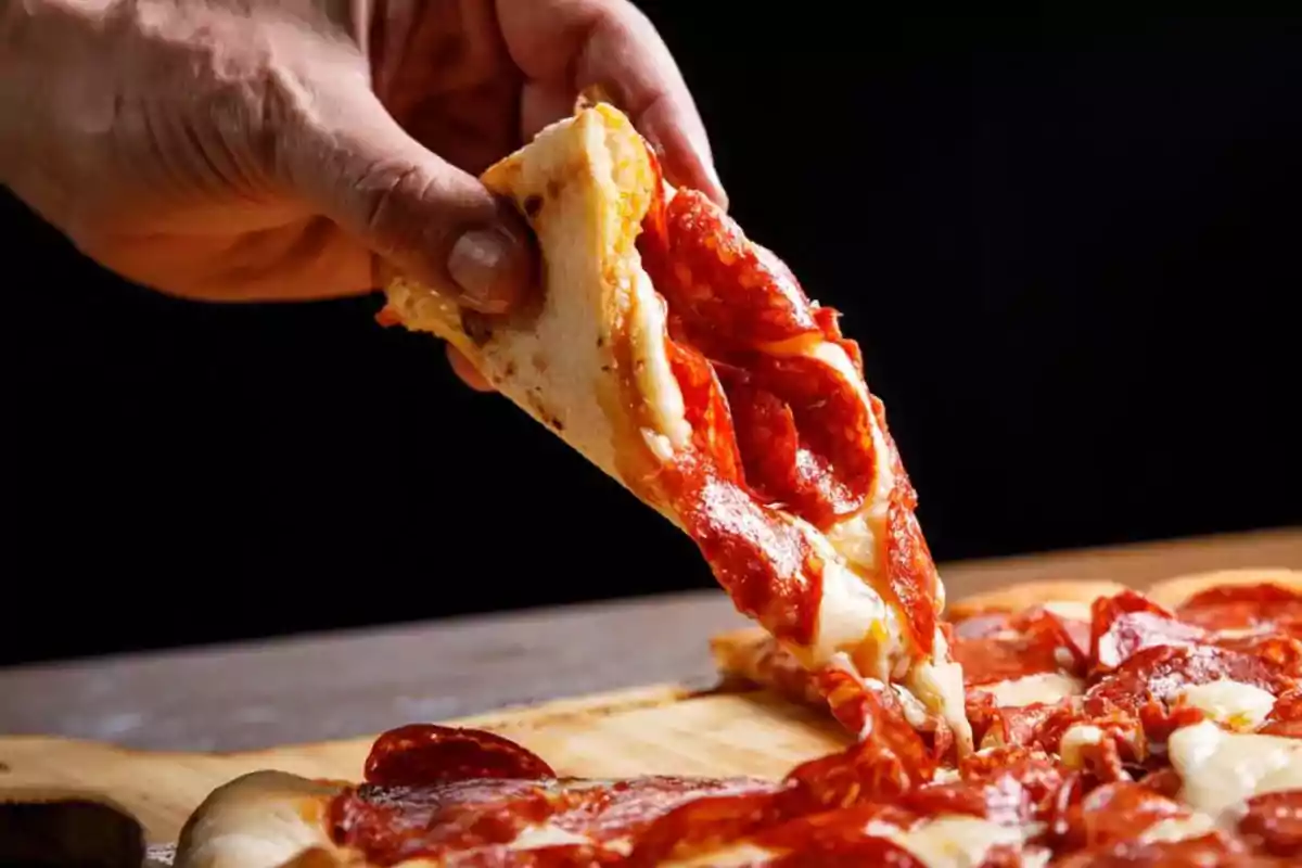 Hand lifting a slice of pepperoni pizza with melted cheese Hand lifting a slice of pepperoni pizza with melted cheese