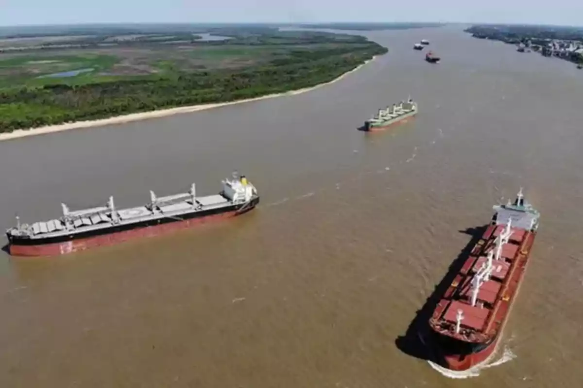 Vista aérea de varios barcos navegando por un río ancho con vegetación en las orillas.