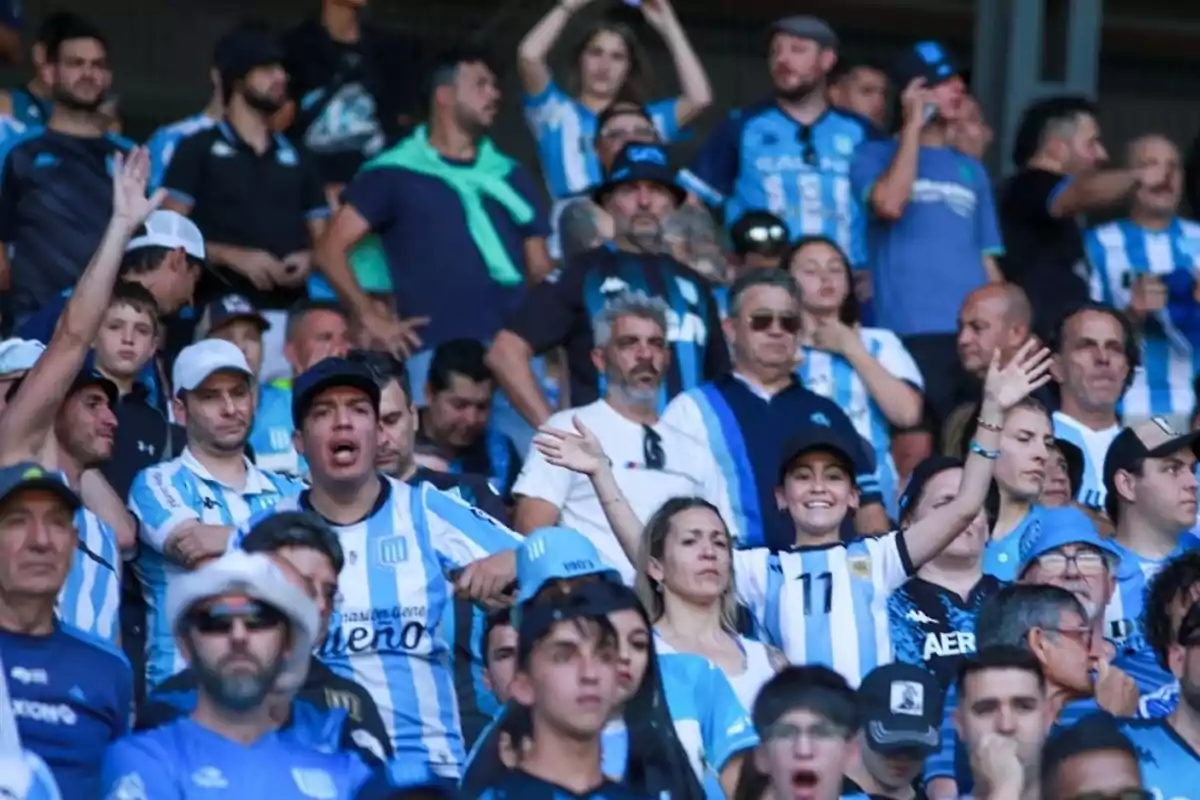 Aficionados de fútbol con camisetas a rayas celestes y blancas animan desde las gradas.