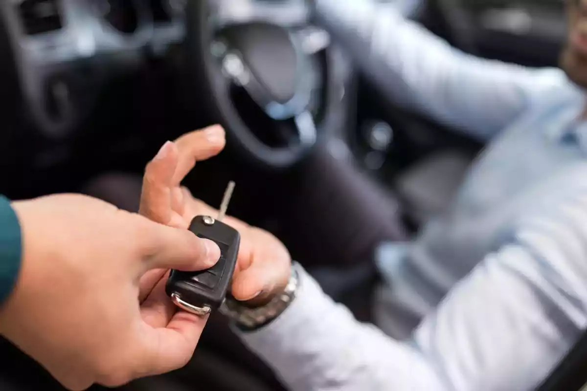Person handing car keys to someone sitting in the driver's seat