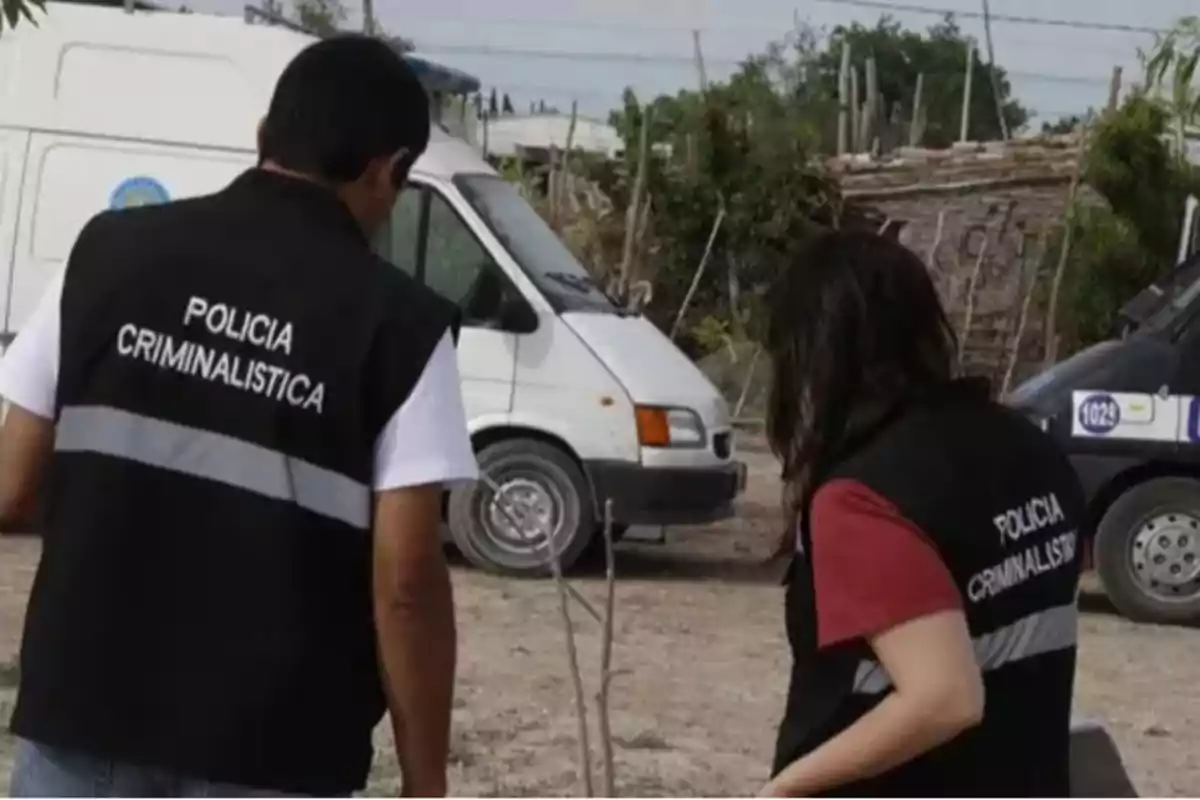 Dos personas con chalecos de "Policía Criminalística" están de pie cerca de una furgoneta blanca en un entorno al aire libre.