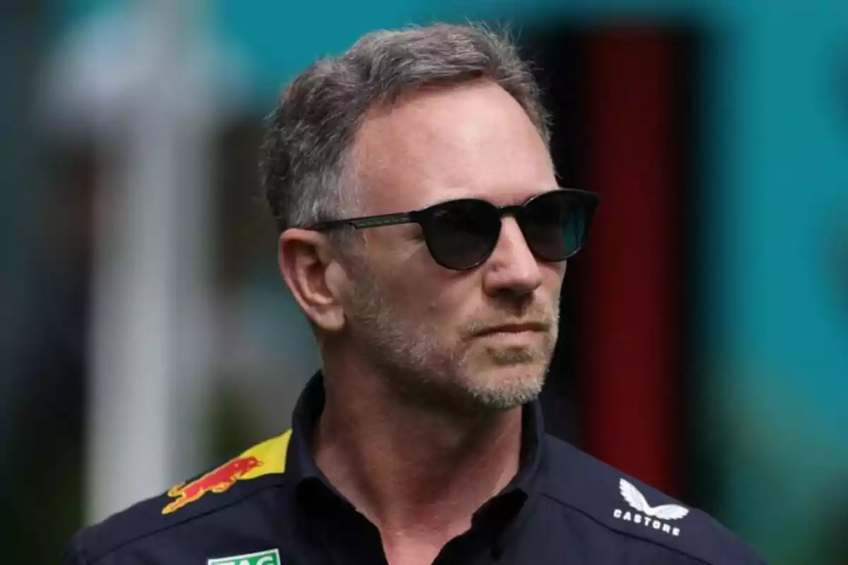 Un hombre con gafas de sol y barba corta lleva una camisa oscura con logotipos coloridos. Un hombre con gafas de sol y barba corta lleva una camisa oscura con logotipos coloridos.
