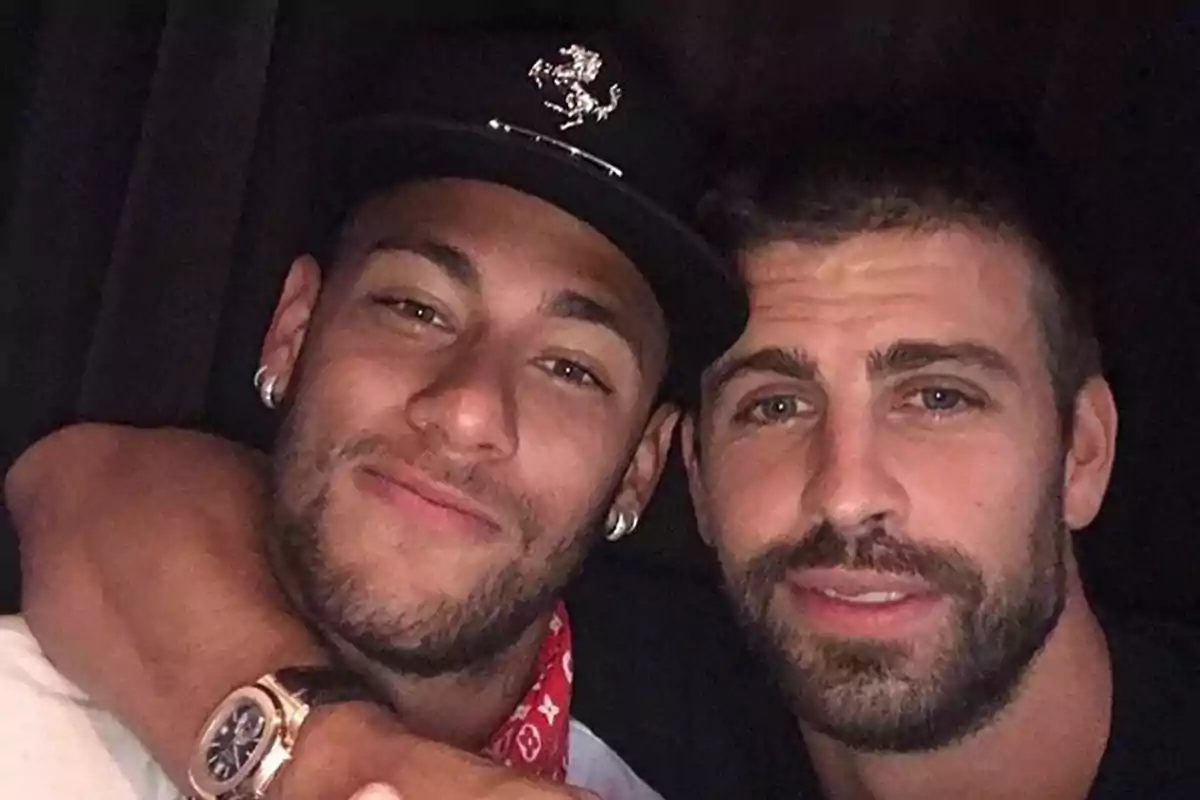 Dos hombres posan juntos para una selfie, uno lleva gorra negra y reloj, el otro tiene barba y ambos sonríen levemente.