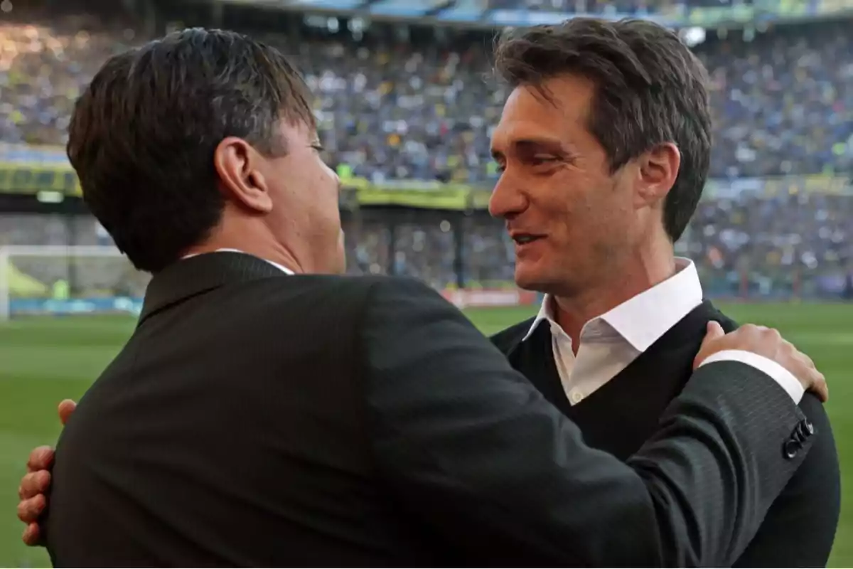 Two men greet each other amicably in a soccer stadium full of spectators.