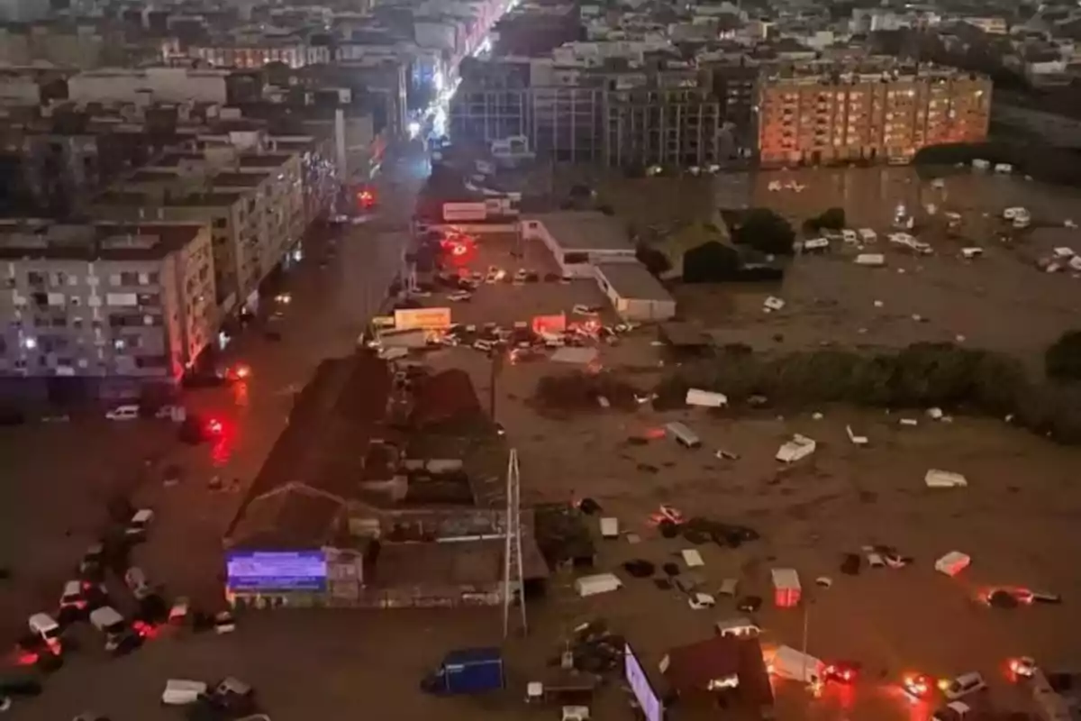 Vista aérea de una ciudad inundada durante la noche con luces de vehículos reflejándose en el agua.