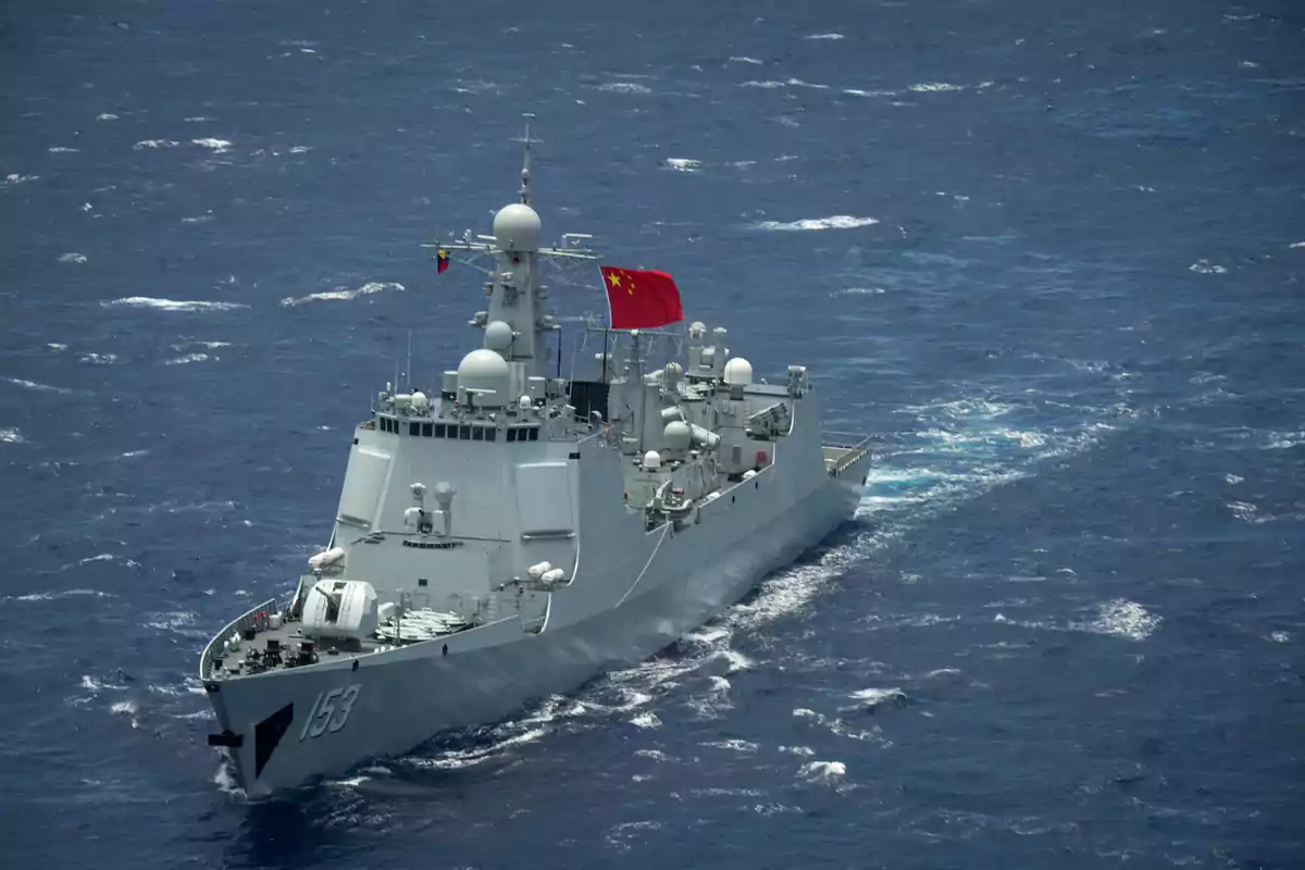 Un buque de guerra navegando en el océano con una bandera roja ondeando en la parte superior.