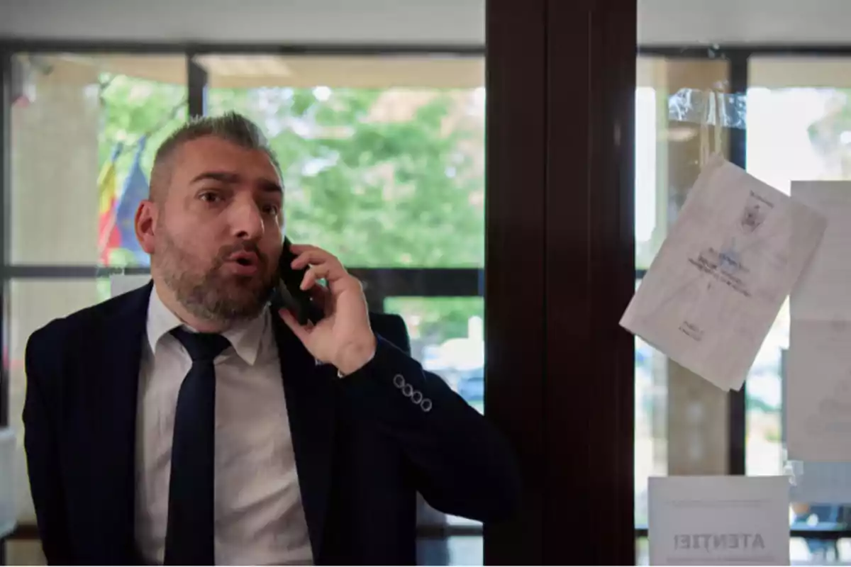 Un hombre con traje y corbata está hablando por teléfono móvil frente a una puerta de vidrio con papeles pegados. Un hombre con traje y corbata está hablando por teléfono móvil frente a una puerta de vidrio con papeles pegados.