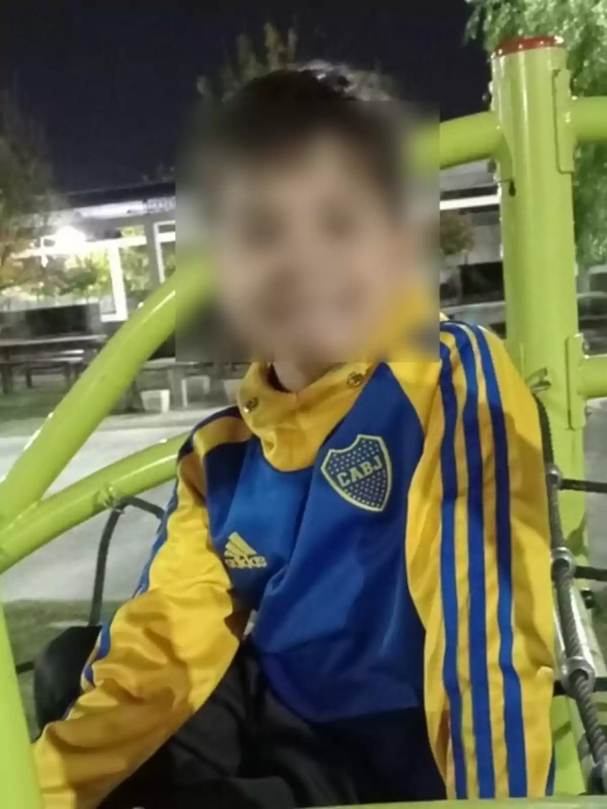 Niño con buzo azul y amarillo de Boca Juniors sentado en un juego de plaza por la noche Niño con buzo azul y amarillo de Boca Juniors sentado en un juego de plaza por la noche