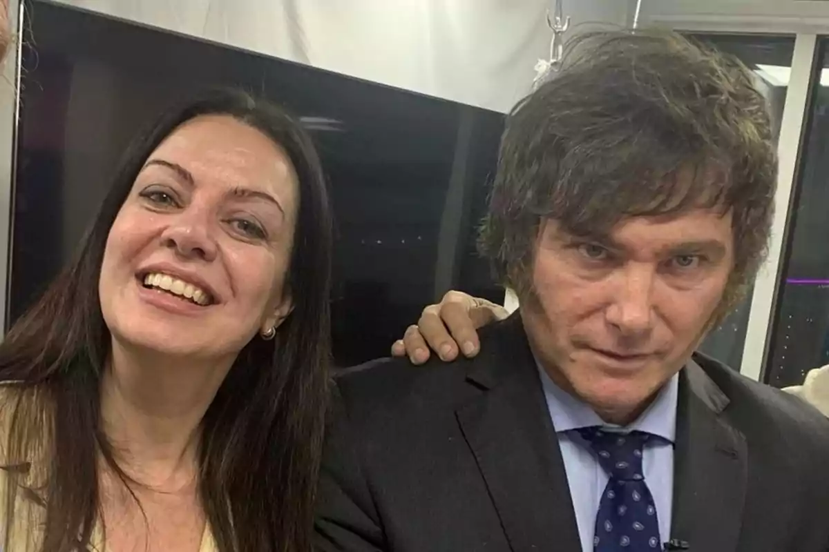 Dos personas posando juntas, una mujer sonriente y un hombre con expresión seria, ambos en un entorno interior.