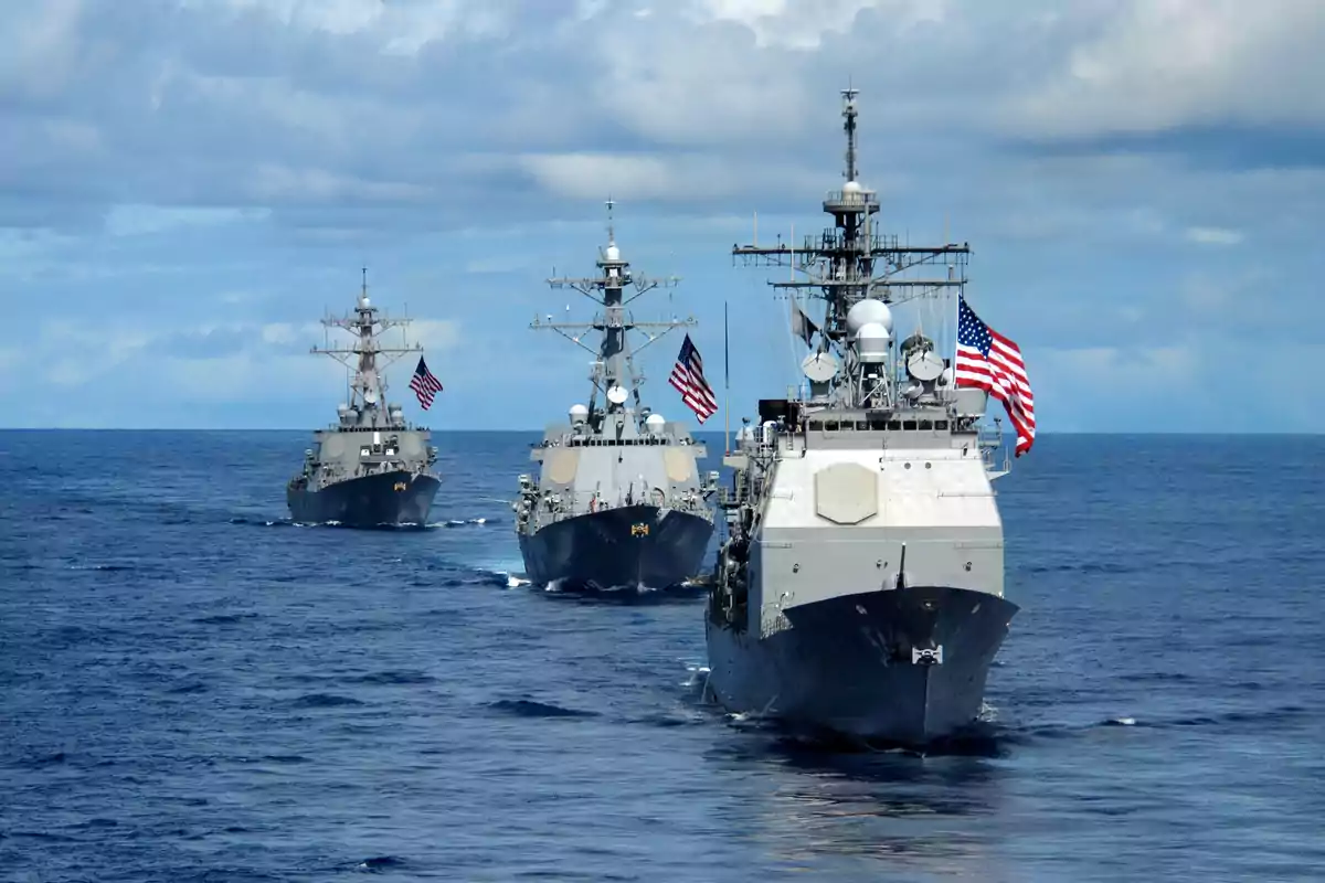Three warships sailing in formation in the ocean with flags waving.