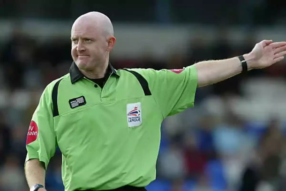 A soccer referee in a green uniform pointing with an outstretched arm on a playing field.