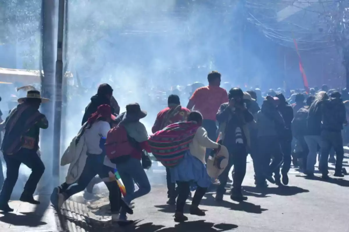 A group of people is running on a smoke-filled street, some wearing colorful clothes and hats.
