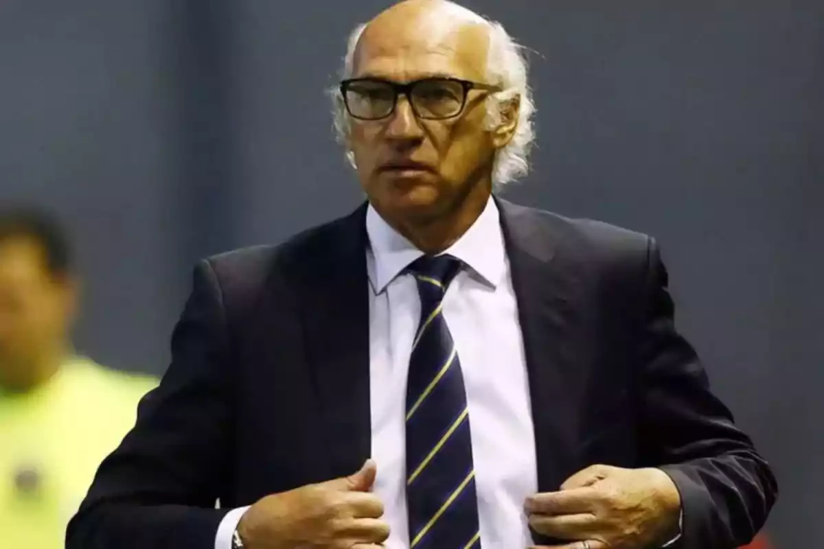 Un hombre de cabello canoso y gafas viste un traje oscuro con corbata a rayas. Un hombre de cabello canoso y gafas viste un traje oscuro con corbata a rayas.