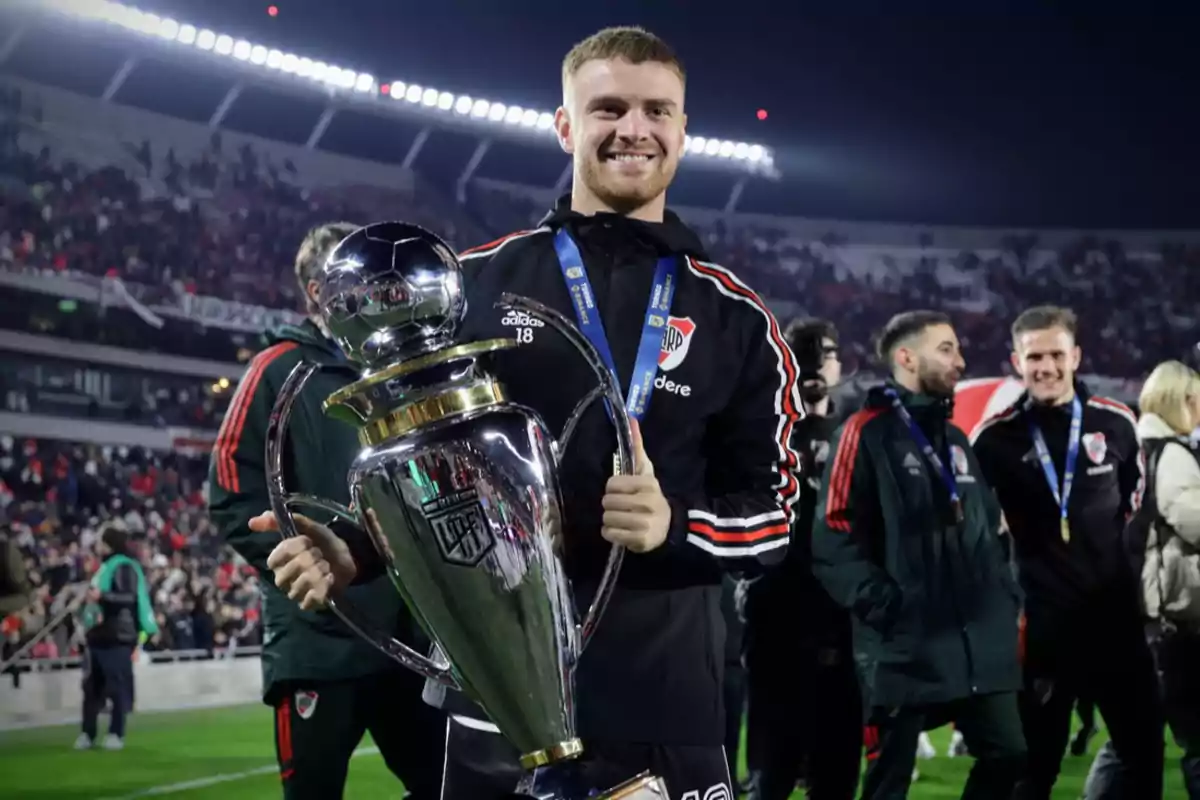 A player smiles while holding a trophy in a stadium full of spectators. A player smiles while holding a trophy in a stadium full of spectators.